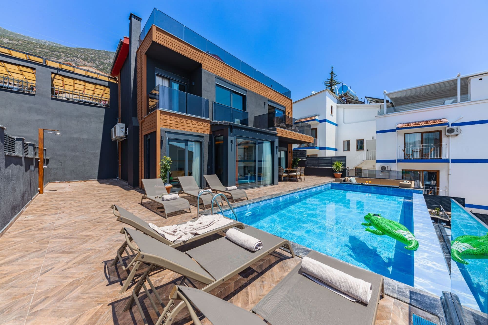 Villa terrace with rows of sun loungers beside a pool with an inflatable crocodile