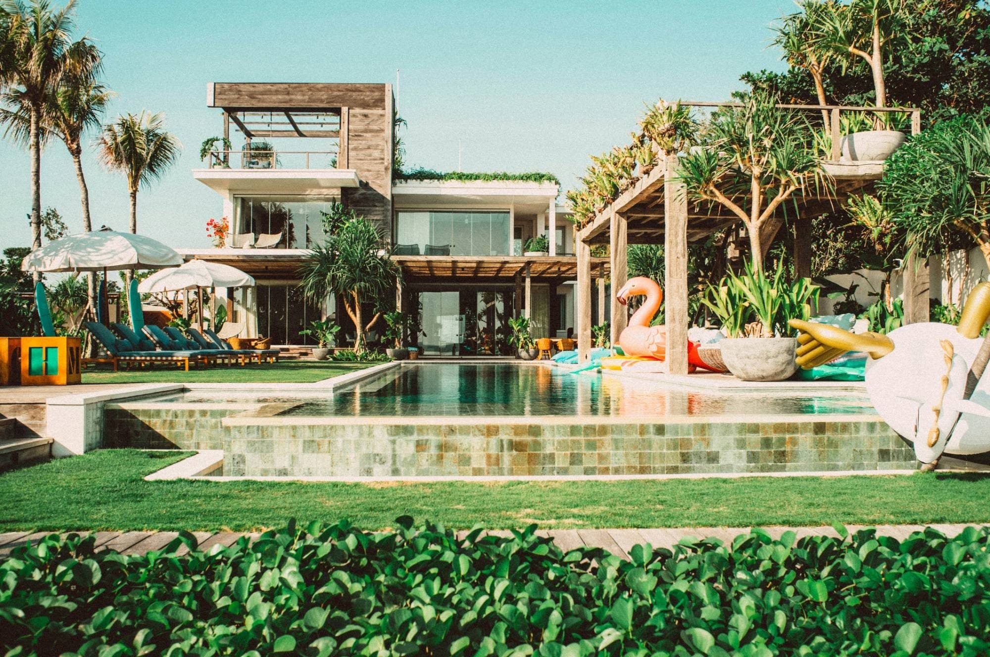 Large modern villa with a long pool, lawn, sun loungers and an inflatable flamingo